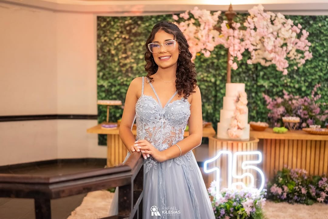 Debutante Duda em vestido de festa em frente a um letreiro neon com o número 15