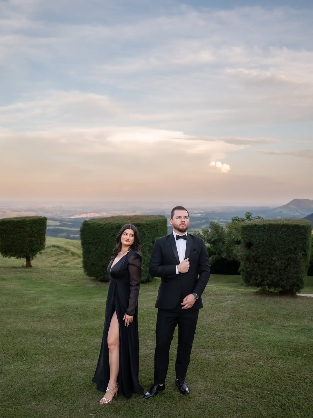 Casal em trajes formais posando nas colinas ao entardecer, luz dourada de pré-wedding