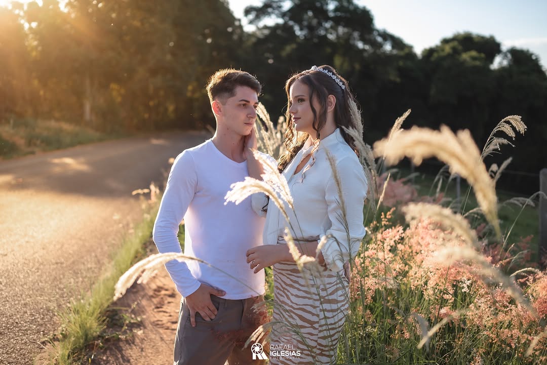 Casal Heloísa e Matheus em contraluz dourada numa estrada de terra em meio ao campo